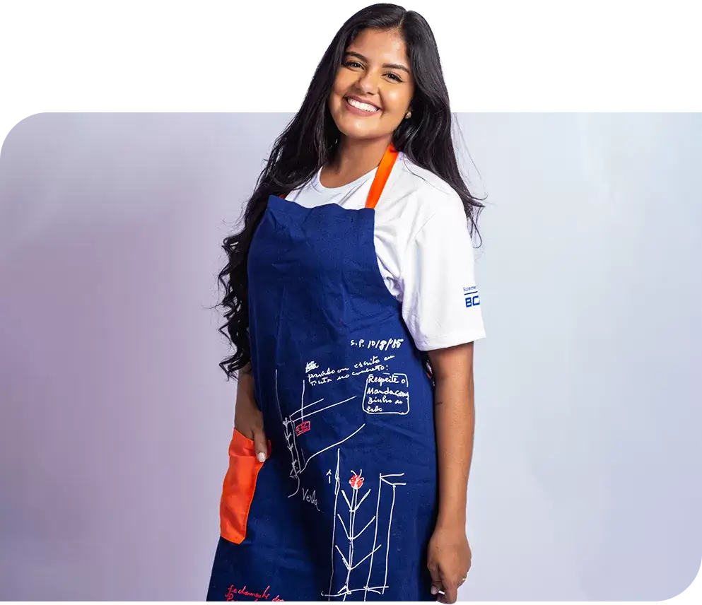 SP< Uniformes - Mulher vestindo camiseta gola redonda manga curta e avental com cores contrastantes e estampa frontal.